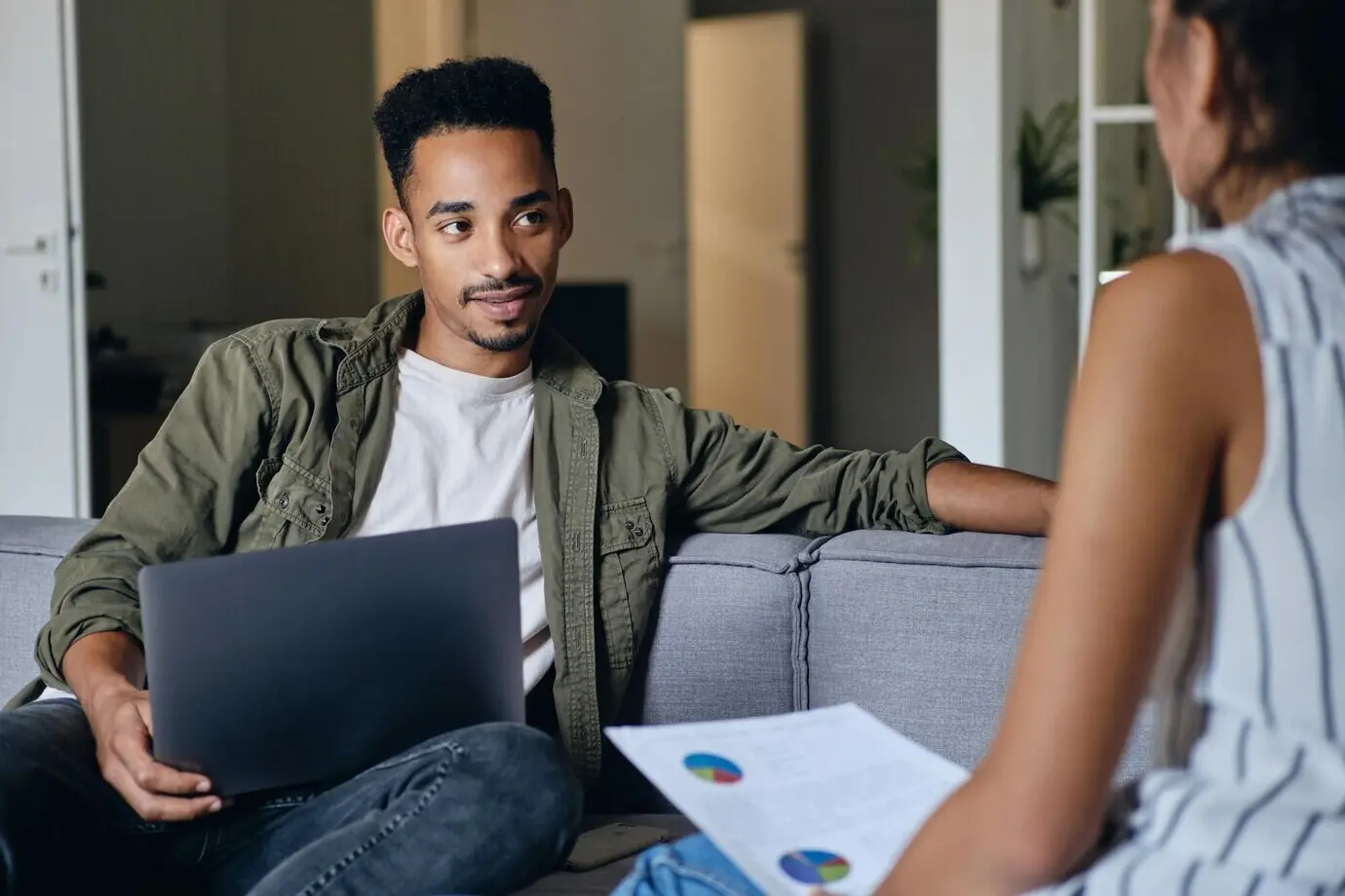A young, attractive African American man using a laptop while collaborating with a colleague in a modern coworking space.